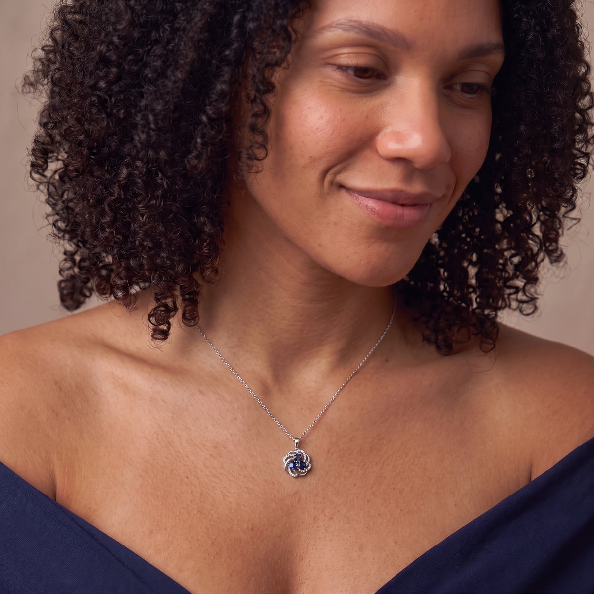 Woman in a navy off-shoulder top wearing a blue sapphire three stone necklace
