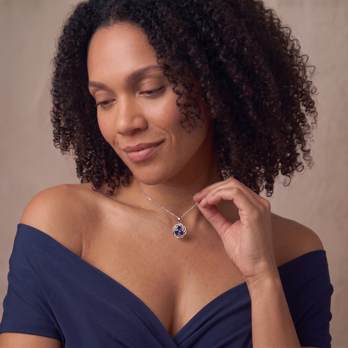 Woman holding a September birthstone sapphire pendant necklace at her collarbone