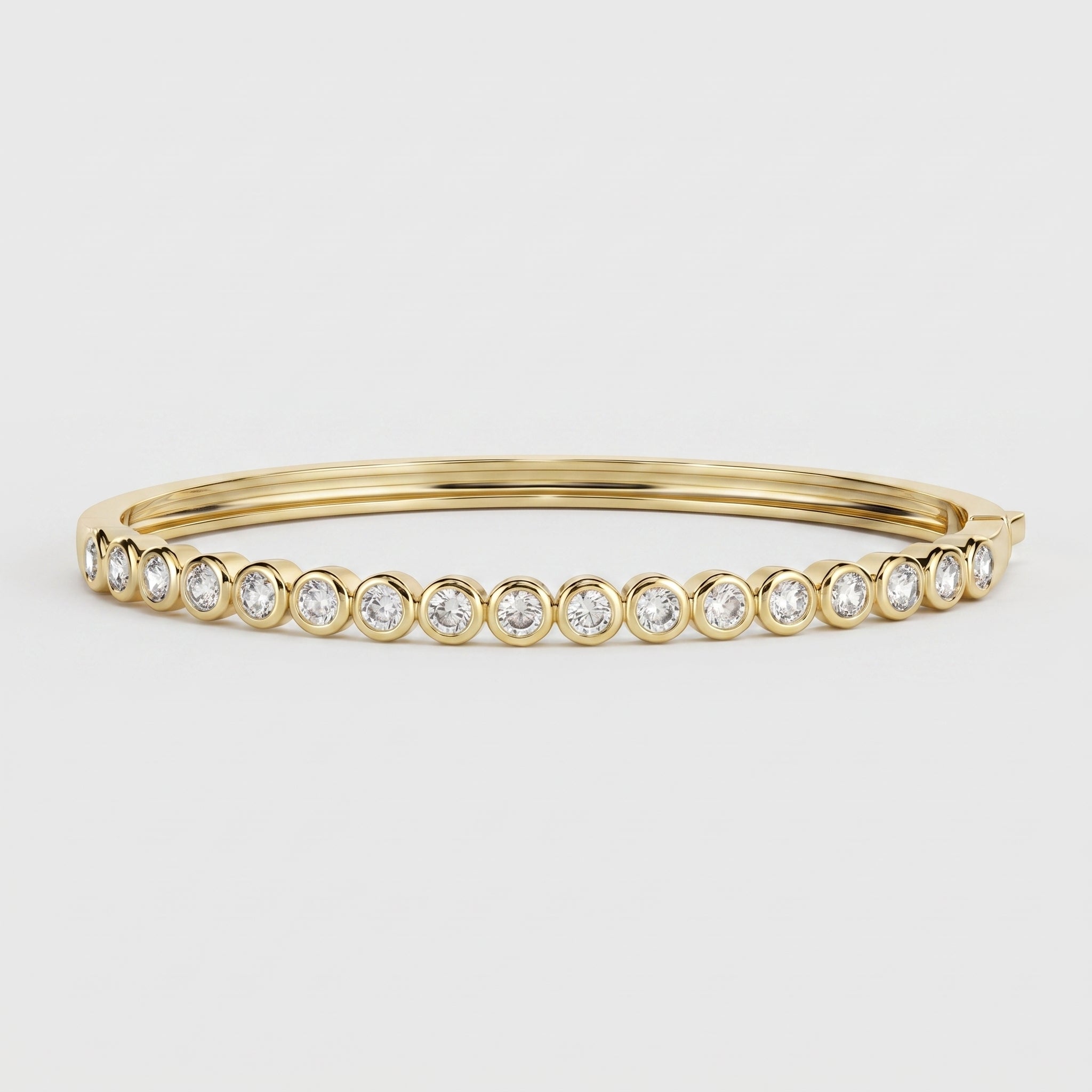 A gold bangle bracelet featuring a row of round-cut clear gemstones in bezel settings, photographed on a clean light gray background.