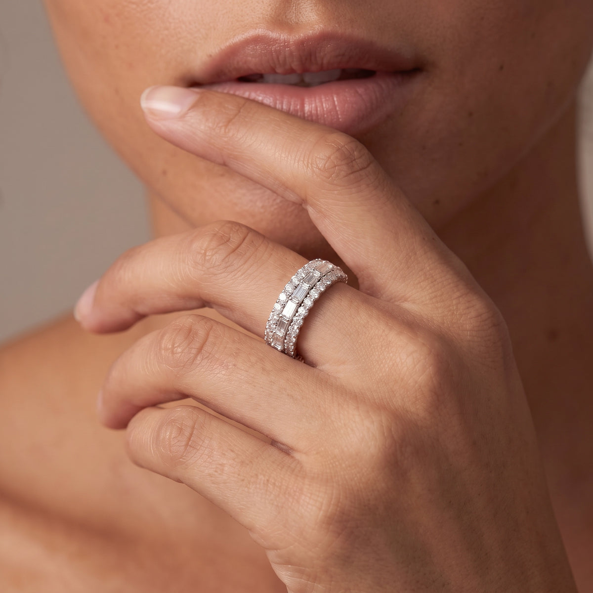Hand at the lips wearing a wide round and baguette lab diamond band in white gold plated silver