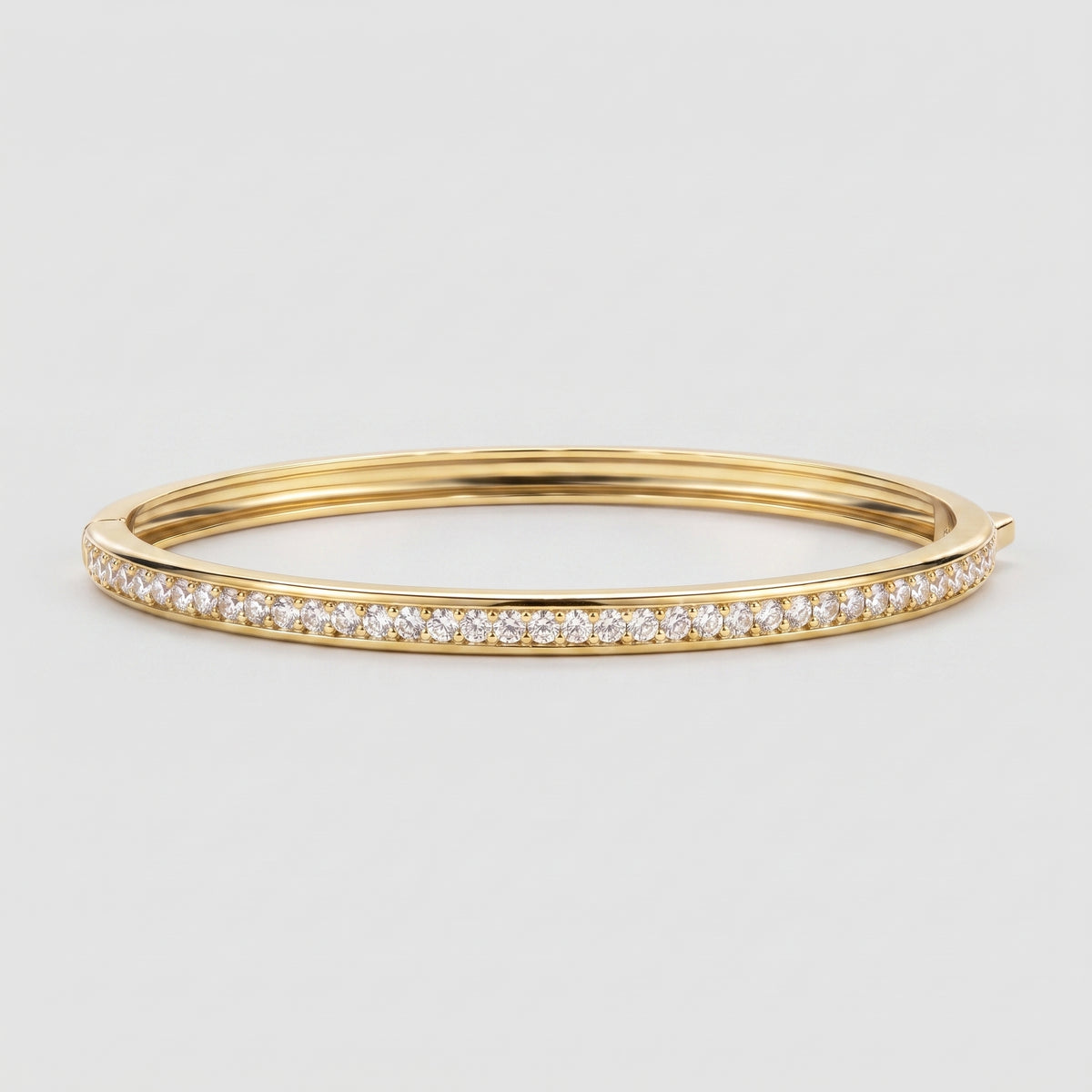 A gold hinged bangle bracelet featuring a single row of pavé-set round diamonds along the front edge, shown against a light gray background.