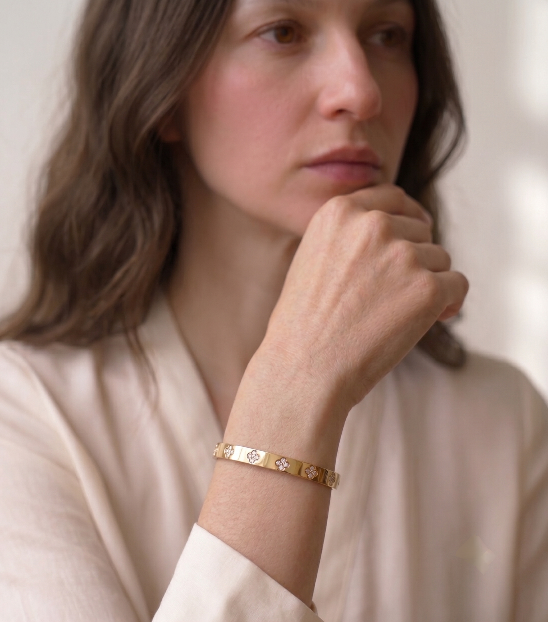 Gold clover bangle bracelet with moissanite worn on the wrist with a soft cream silk shirt