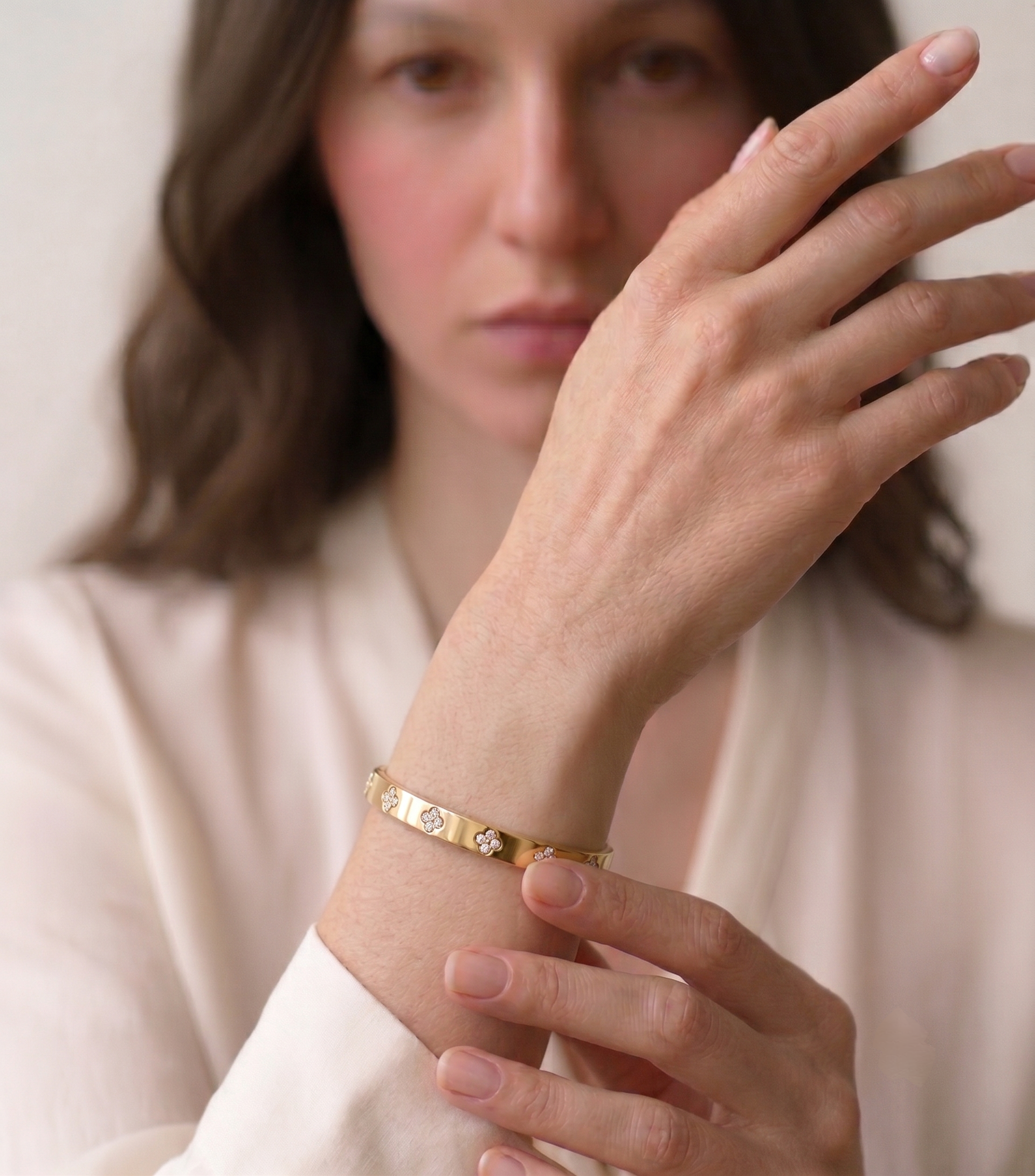 Woman in a cream blouse wearing the MH Elegance gold plated four leaf clover bangle bracelet with moissanite stones