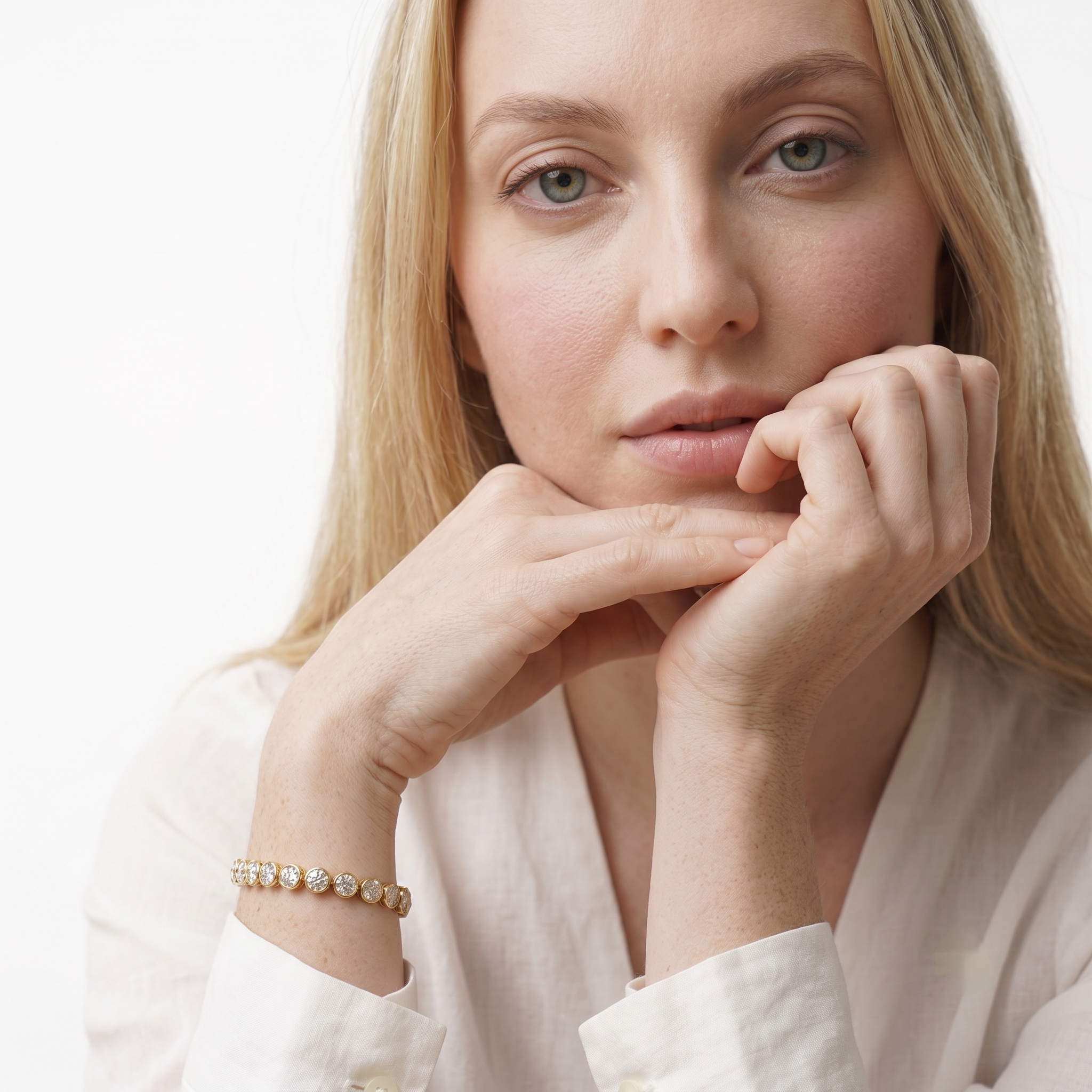 Woman resting her chin on her hand showing the gold bangle bracelet with round bezel-set cubic zirconia stones