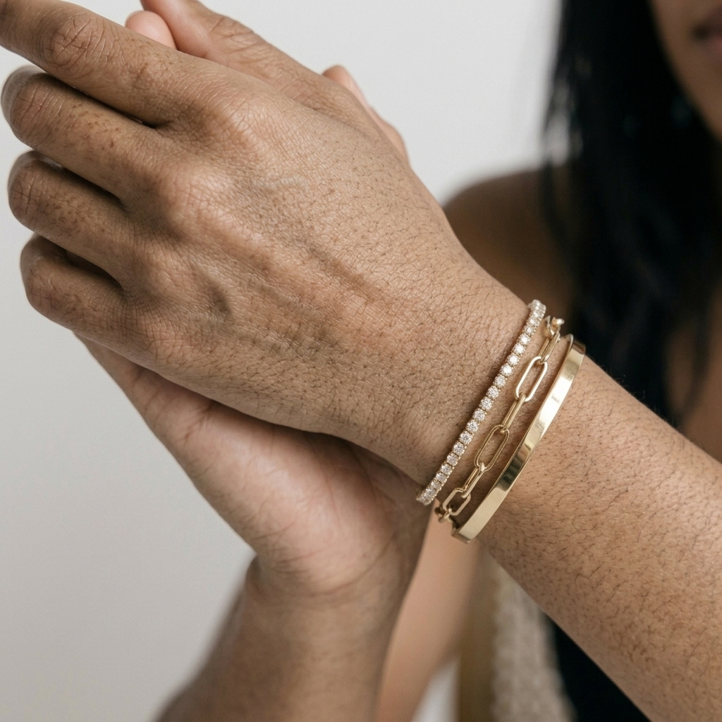 Close view of a gold plated CZ tennis bracelet, paperclip chain and smooth bangle on a wrist