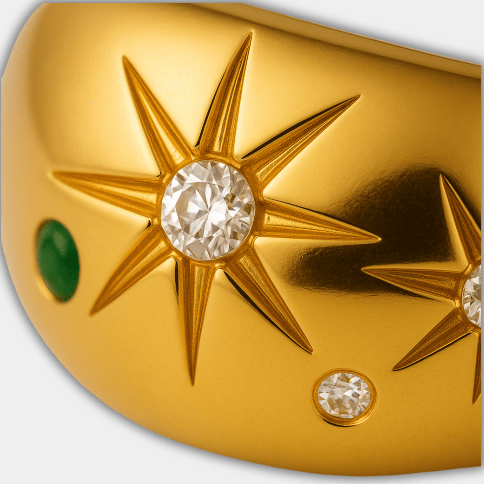 Macro close-up of one starburst medallion with a clear zircon center stone and green accent gem on the gold band