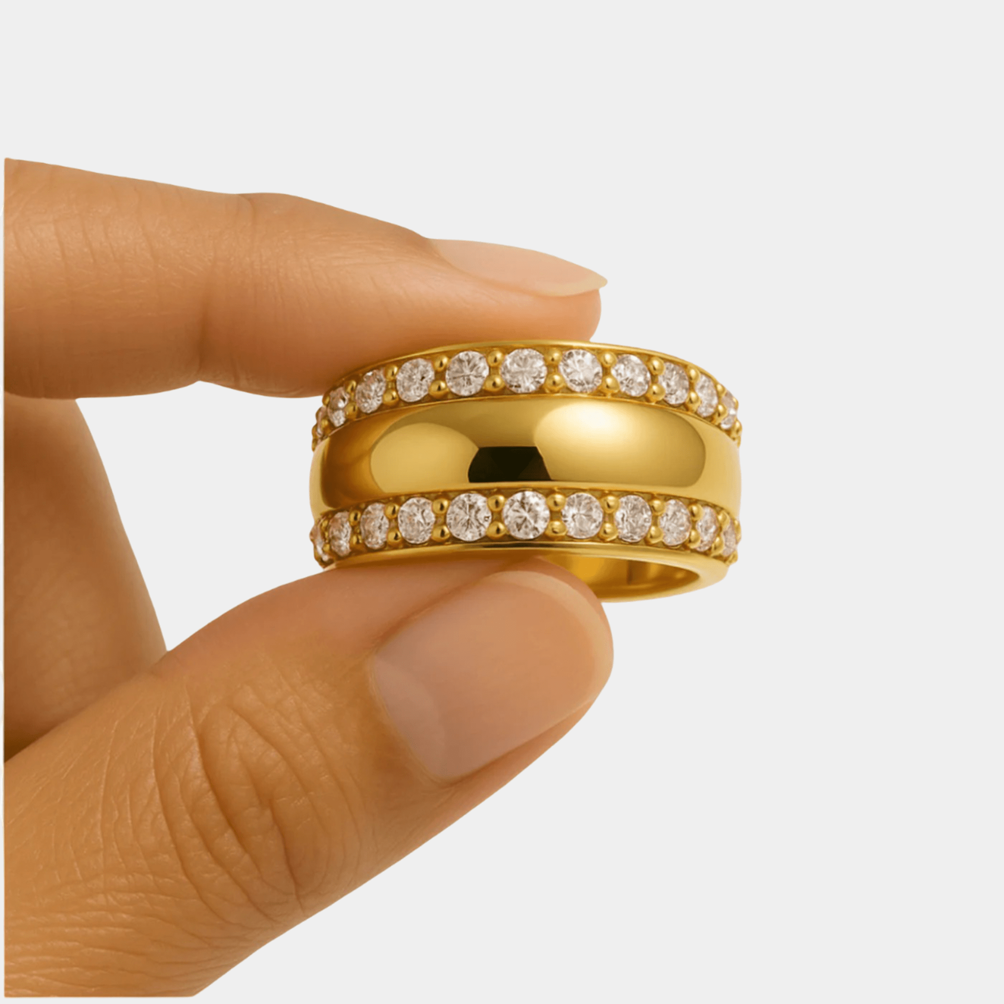 Gilded zircon band ring held between two fingers to show its scale and polished gold finish