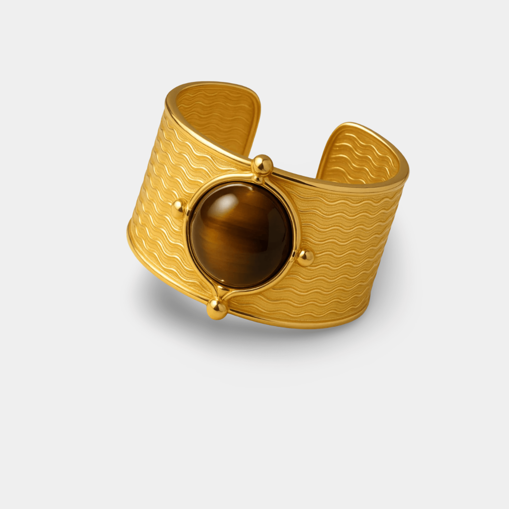 Heritage tiger's eye cuff ring with a golden brown cabochon on a wave-textured 18K gold plated band, angled view