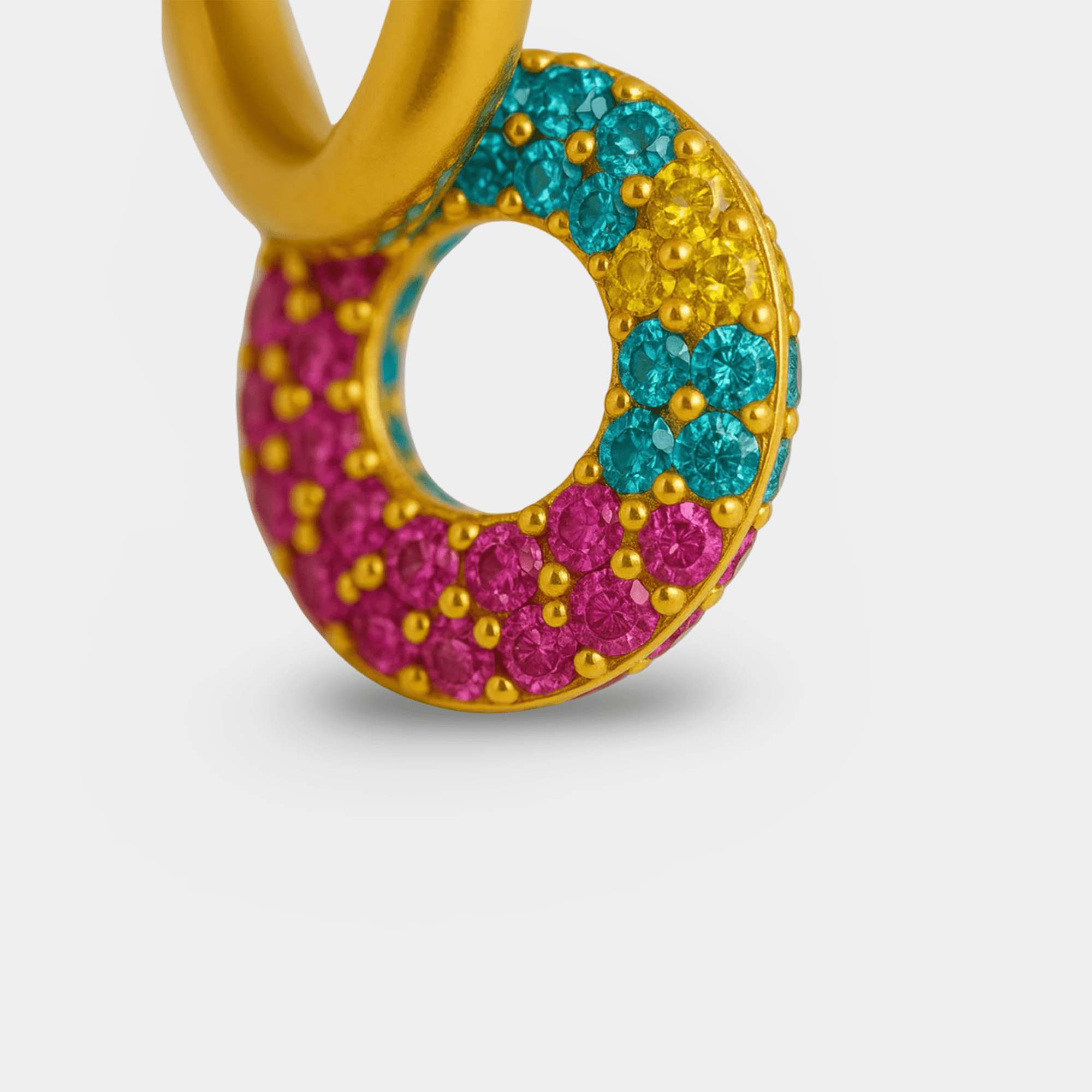 Macro close-up of pavé cubic zirconia donut charm in pink, turquoise, and yellow on a gold plated hoop earring